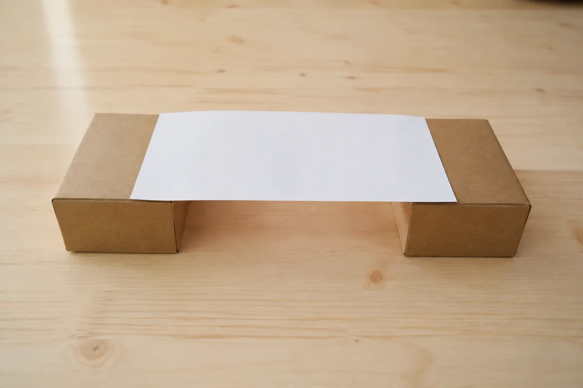 Étape 1 : feuille plate reliant deux boîtes à écart mesuré, pour « Construire un pont solide avec des tubes de papier roulé ».