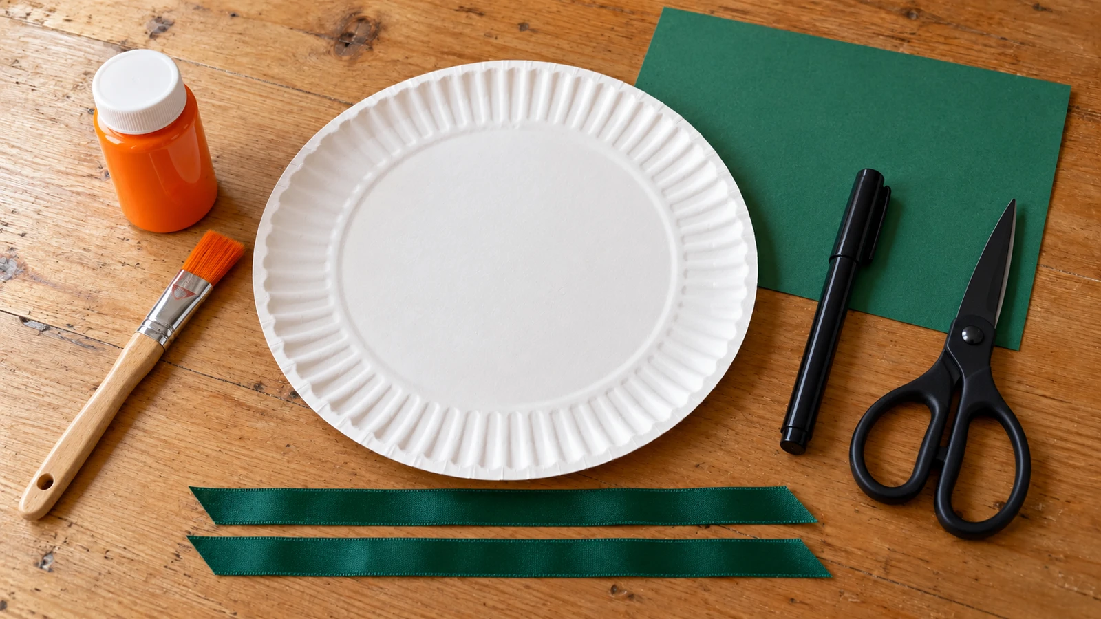 Assiette, couleur orange, carton vert et ciseaux disposés pour le masque citrouille