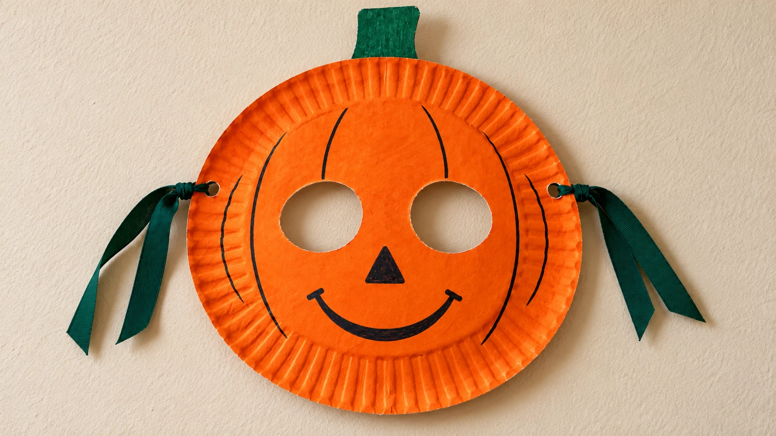 Masque citrouille orange fabriqué avec une assiette et une tige verte en carton