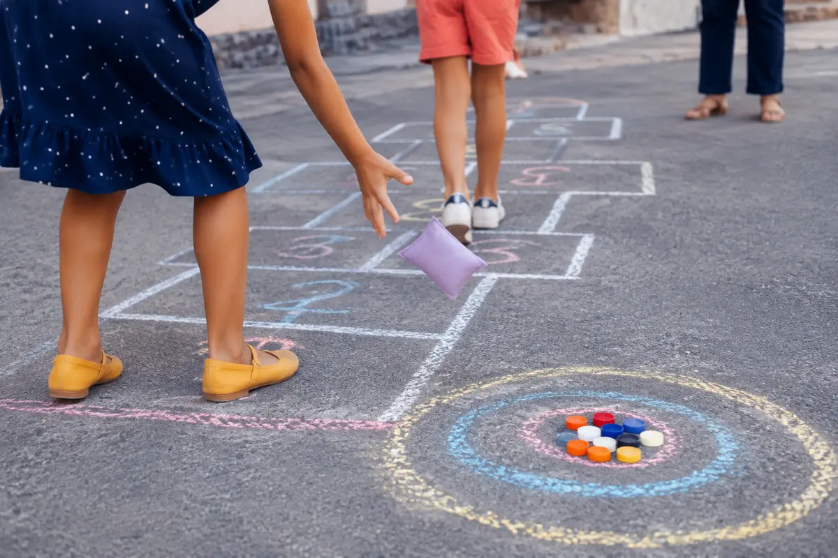 Enfants jouant à une marelle tracée à la craie et lançant un palet plat