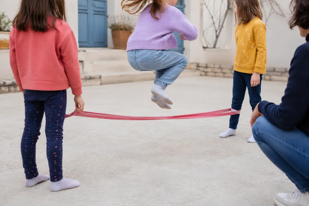 Enfants sautant à la corde sur une surface plane avec un adulte à proximité