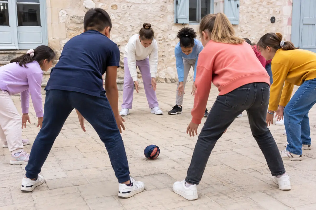 Enfants en cercle faisant rouler une balle textile dans le jeu de la tomate