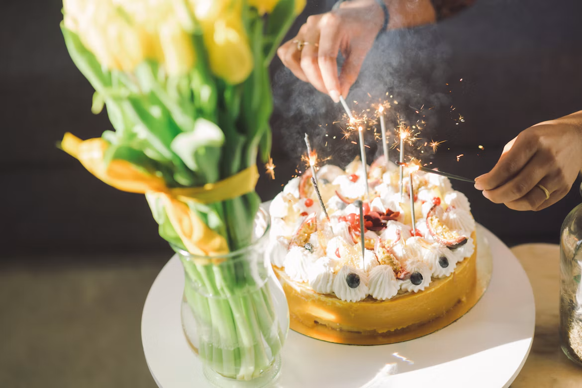 Tulipes jaunes dans un vase à côté d'un gâteau d'anniversaire avec des cierges magiques